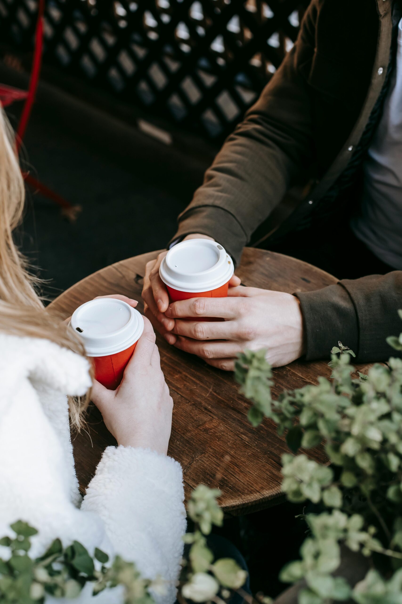Crop faceless couple having date with takeaway beverage on wooden terrace of cafeteria